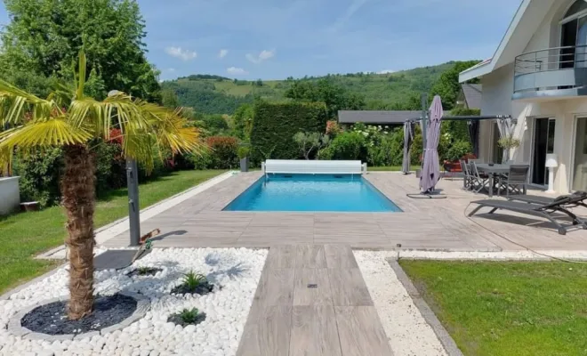 Découvrez le résultat final de notre savoir-faire : une piscine contemporaine parfaitement intégrée à son environnement paysager. Autour de l'eau cristalline, nous avons réalisé une superbe plage en carrelage aspect bois chaleureux, prolongée par un espace zen en galets blancs orné d'un palmier. Un aménagement extérieur complet et haut de gamme, pensé pour sublimer votre jardin.  Prenez contact avec Electron TP dès à présent : [node:title] à [soref:zone_pr].